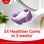 Angled toothbrush head with purple bristles and toothpaste foam in a bathroom setting, Colgate logo and '3X Healthier Gums in 3 weeks' text.