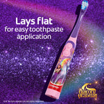 Purple Colgate Unicorn Academy electric toothbrush on glittery purple background with text stating it lays flat for easy toothpaste application.