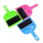 Top-down view of three colorful handheld dustpan-and-brush sets in green, pink, and blue with black bristles on a white background.