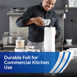 Smiling worker wrapping food with aluminum foil in a commercial kitchen, foil-wrapped containers on counter
