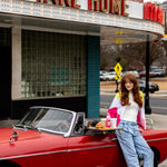 Young woman leaning on a red convertible with a tray of burger and fries and a visible Citrus Magic Dragonfruit spray bottle