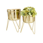 Two gold metal planters on stands, one filled with green hydrangea-like faux flowers, on white background