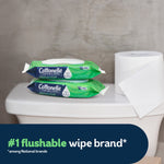 Two green Cottonelle GentlePlus flushable wipes packs on a toilet tank next to a roll of toilet paper and brand caption