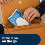 Hand placing a blue Cottonelle Fresh Care flip-top wipes pack into a tan handbag, highlighting portability