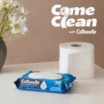 Blue Cottonelle Fresh Care wipes pack staged on a surface beside a toilet paper roll and floral vase with 'Come Clean' branding