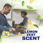 Couple cleaning a kitchen together with a Mr. Clean Clean Freak lemon zest spray in foreground and floating lemon graphics and leaves.