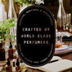 Oval black sign reading crafted by world-class perfumers over a blurred apothecary-style background