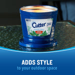 Blue Cutter outdoor candle on a glass table top with warm glow and promotional text ‘adds style’.