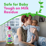 Lifestyle image with a Dapple bottle and baby bottle on a table in foreground and a mother holding and kissing a baby in the background