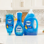 Lifestyle photo of three Dawn cleaning products, including a large refill jug and smaller bottles, arranged on a kitchen counter.