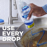 Close-up of a hand tilting an almost-empty Dawn Platinum bottle to pour blue liquid into a heavily soiled pan with 'Use every drop' text