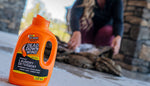 Orange Dead Down Wind laundry detergent bottle in foreground with blurred person in background loading firewood outdoors