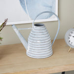 Gray ribbed beehive-shaped metal watering can styled on a wooden table with clock and artwork