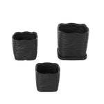 Top-down angled view of three black wavy-ribbed ceramic planters showing open interiors and saucer