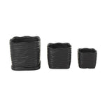 Front-facing studio photo of three stacked-size black wavy-ribbed ceramic planters with saucer