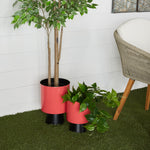 Pair of red metal planters with black bases staged on artificial grass beside a chair and wall for lifestyle display