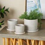 Styled trio of DecMode white ceramic planters with grid pattern and brown rims displayed on a table with faux plants and artwork behind