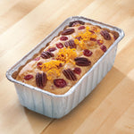 Baked loaf topped with pecans, cranberries and orange zest in an aluminum mini loaf pan on a wooden surface
