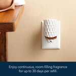 White decorative plug-in diffuser inserted in an electrical outlet on a beige wall beside a wooden table edge.