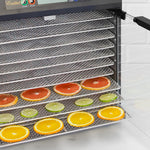 Close-up of an electric food dehydrator interior with stacked wire trays holding sliced citrus fruits ready for drying.