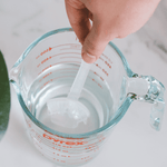 Hand holding a dental guard on a stirring tool being immersed into a Pyrex measuring cup of hot water for molding