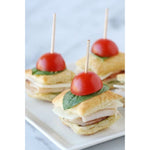 Close-up appetizer bites skewered with wooden toothpicks topped with halved cherry tomatoes and basil