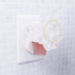 Plug-in fragrance diffuser inserted in an outlet with a clear decorative crystal attachment and a visible pink oil refill bottle.