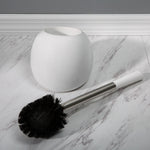 Toilet brush with stainless handle and detached white dome holder lying on marble-patterned tile