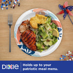 Top-down lifestyle image of a Dixie floral paper plate on a wood table holding grilled chicken, salad and a biscuit with patriotic confetti.