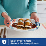 Hands presenting a Dixie floral-patterned paper plate filled with two enchiladas and rice on a kitchen counter.