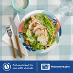Overhead plate setting with a Caesar-style salad on a Dixie patterned paper plate, utensils and a drink at the table.