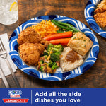 Blue-wave bordered Dixie Ultra paper plate served with fried chicken, sides and a glass on a wood table to show plate capacity