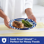 Person presenting a Dixie Ultra blue-swirl paper plate with chicken and asparagus over a table with a yellow runner