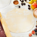 Rolled-out dough on a sheet of parchment paper with a wooden rolling pin, figs, pears and baking ingredients at the edges.