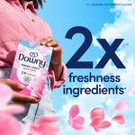 Person holding a Downy April Fresh box in front of a blue sky background with bold '2x freshness ingredients' text and falling petals