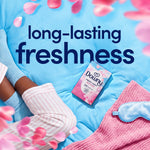 Small Downy April Fresh box on a blue quilt with pajama-clad legs, eye mask and pink petals emphasizing 'long-lasting freshness'
