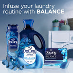 Lifestyle scene showing Downy Balance bottle, Downy Ultra detergent, and Downy infusions sheets near a washing machine