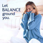 Lifestyle image of a woman in a blue sweater smelling or cuddling the fabric with 'Let BALANCE ground you.' headline.