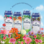 Four Downy Boutique Botanicals scent booster bottles (Peonia, Citrea, Folia, Violeta) displayed among colorful flowers