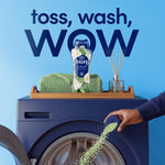 Downy Calm bottle placed on a washer top while green scent beads are poured into the drum in foreground