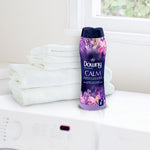 Downy Infusions Calm bottle on a counter next to a stack of white towels by a window in a bright laundry setting