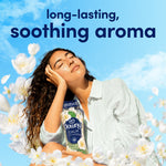 Lifestyle image of person holding a Downy Calm bottle amid floating white flowers under a blue sky