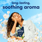 Person reclining against blue sky background holding a Downy CALM box amid floating white flowers and text about soothing aroma