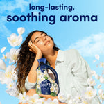 Lifestyle image of a woman holding a Downy Fresh Calm bottle against a blue sky with white flowers and 'soothing aroma' text.