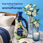 Downy Calm bottle styled on a bedside tray beside vases of white flowers and a lit candle