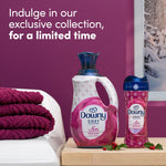 Styled scene showing Downy Cozy Collection bottles next to folded purple towels and snowy window with limited-time collection text