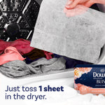 Hand holding a large dryer sheet over clothes inside a dryer drum with packaging corner visible
