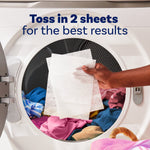 Open dryer door showing laundry and a hand holding two dryer sheets with instruction text about tossing in two sheets