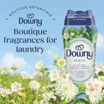 Downy Folia scent booster bottle set against a blue sky with flowers and text reading Boutique fragrances for laundry