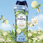 Close-up of a Downy Folia in-wash scent booster bottle with botanical floral artwork on a blue sky background